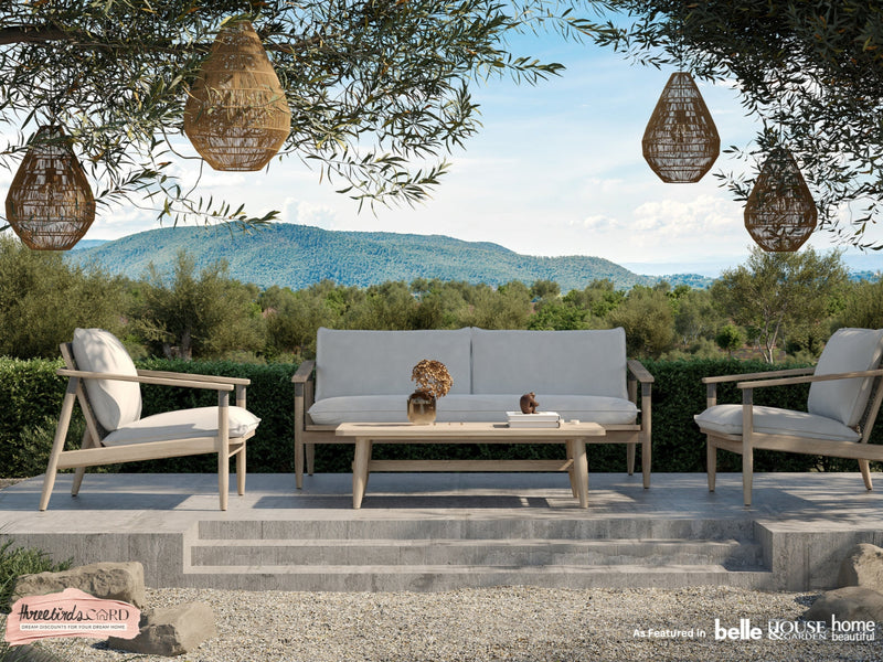 Outdoor patio set with beige sofa, chairs, and coffee table in a scenic setting.